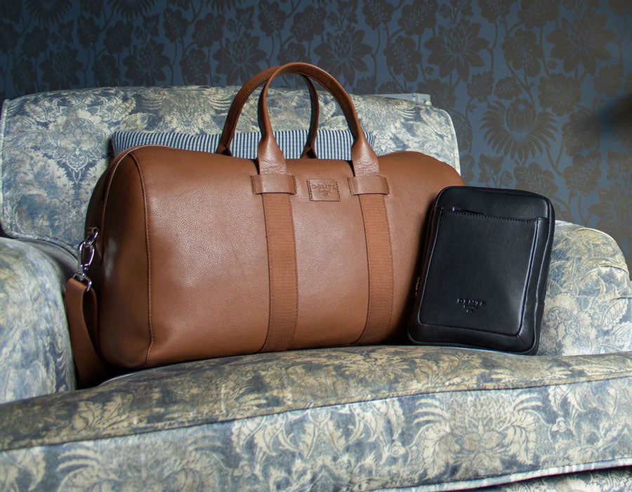 Men's leather bags in various colours laid out on a chair
