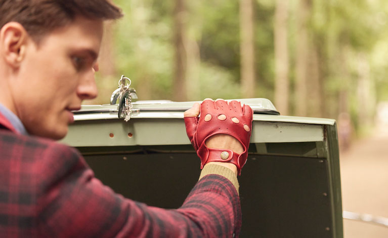 Man wearing leather driving gloves in berry opening the boot of his car